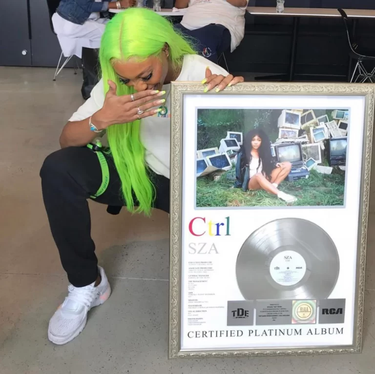 SZA agachada ao lado de seu quadro de certificado de platina.