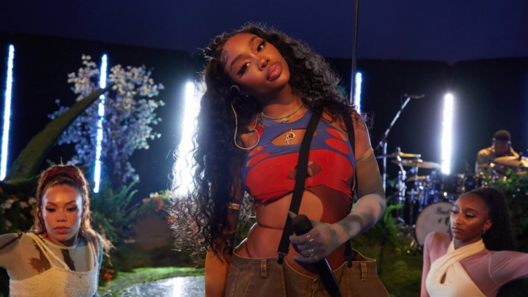 SZA performando no palco com luzes ao fundo.